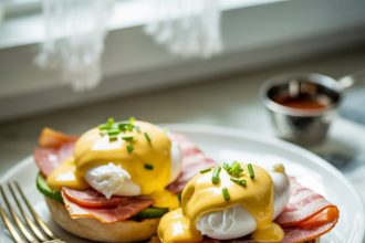 A freshly prepared plate of eggs benedict served with hollandaise sauce and garnished with herbs