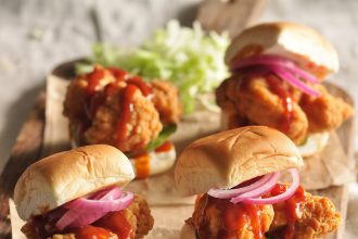 A plate of bang bang chicken sliders with spicy sauce and fresh toppings on mini buns