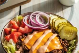 Freshly made cheeseburger bowls with ground beef, cheese, pickles, and lettuce in a white bowl
