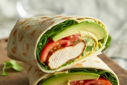 Freshly made chicken avocado wrap with grilled chicken, avocado slices, vegetables, and tortilla on a plate
