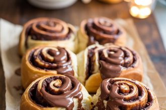 Freshly baked chocolate cinnamon rolls topped with melted chocolate on a wooden board