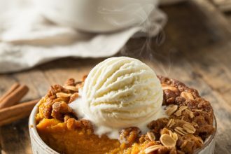 A slice of pumpkin pie crisp topped with whipped cream on a rustic wooden table