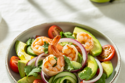 A bowl of fresh shrimp avocado salad with cherry tomatoes, red onions, and lime wedges on a rustic table.